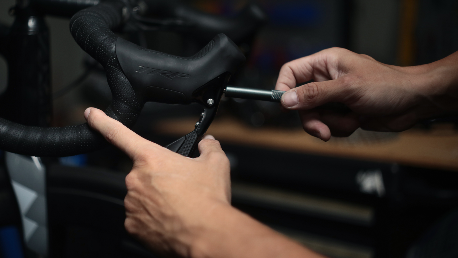 Person adjusting TRP bicycle brake levers with a tool in a workshop setting
