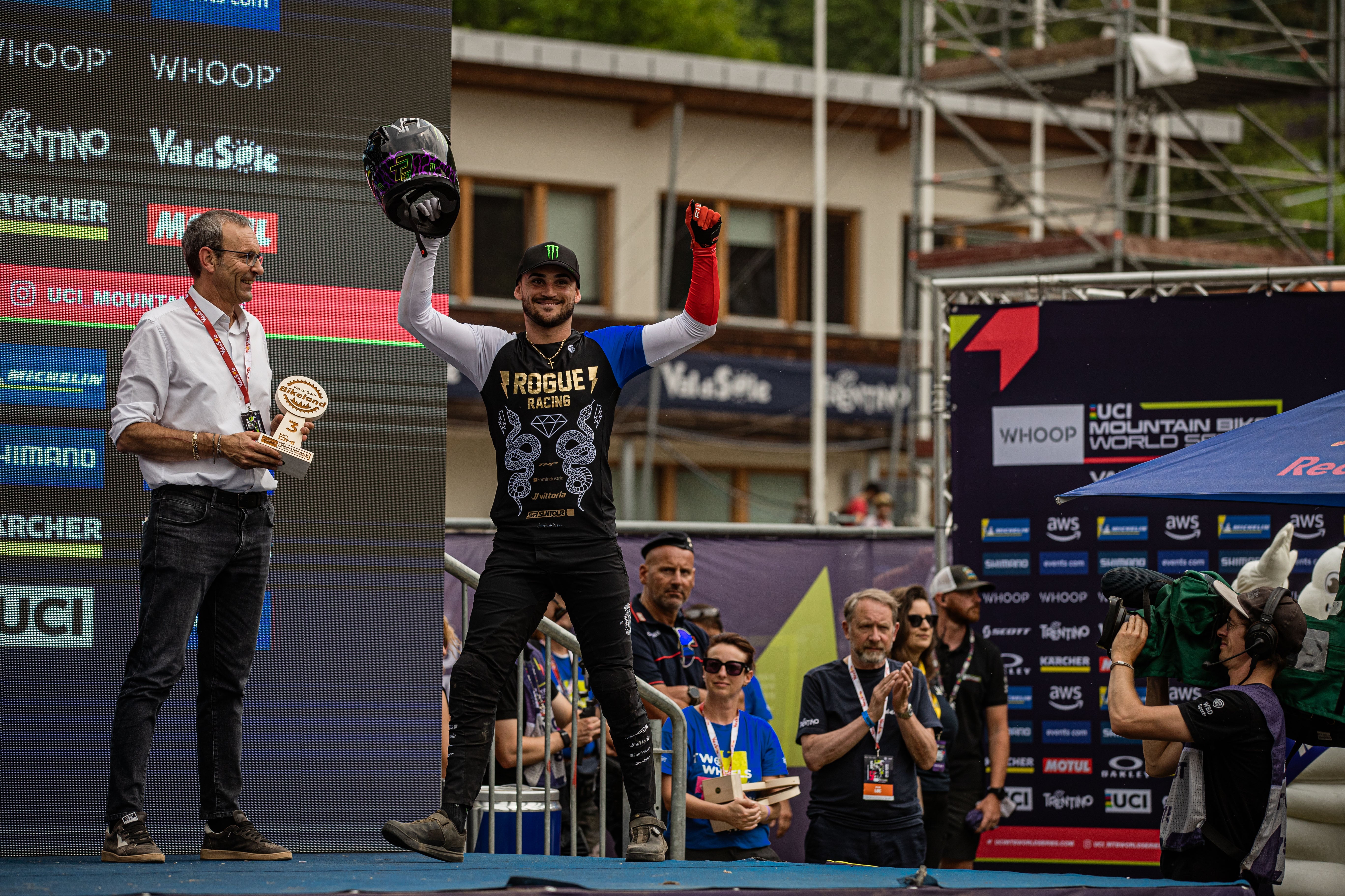 TRP Athlete Thiebaut celebrating on a podium at UCI MTB World Series in Trentino with a large screen displaying event sponsors in the background
