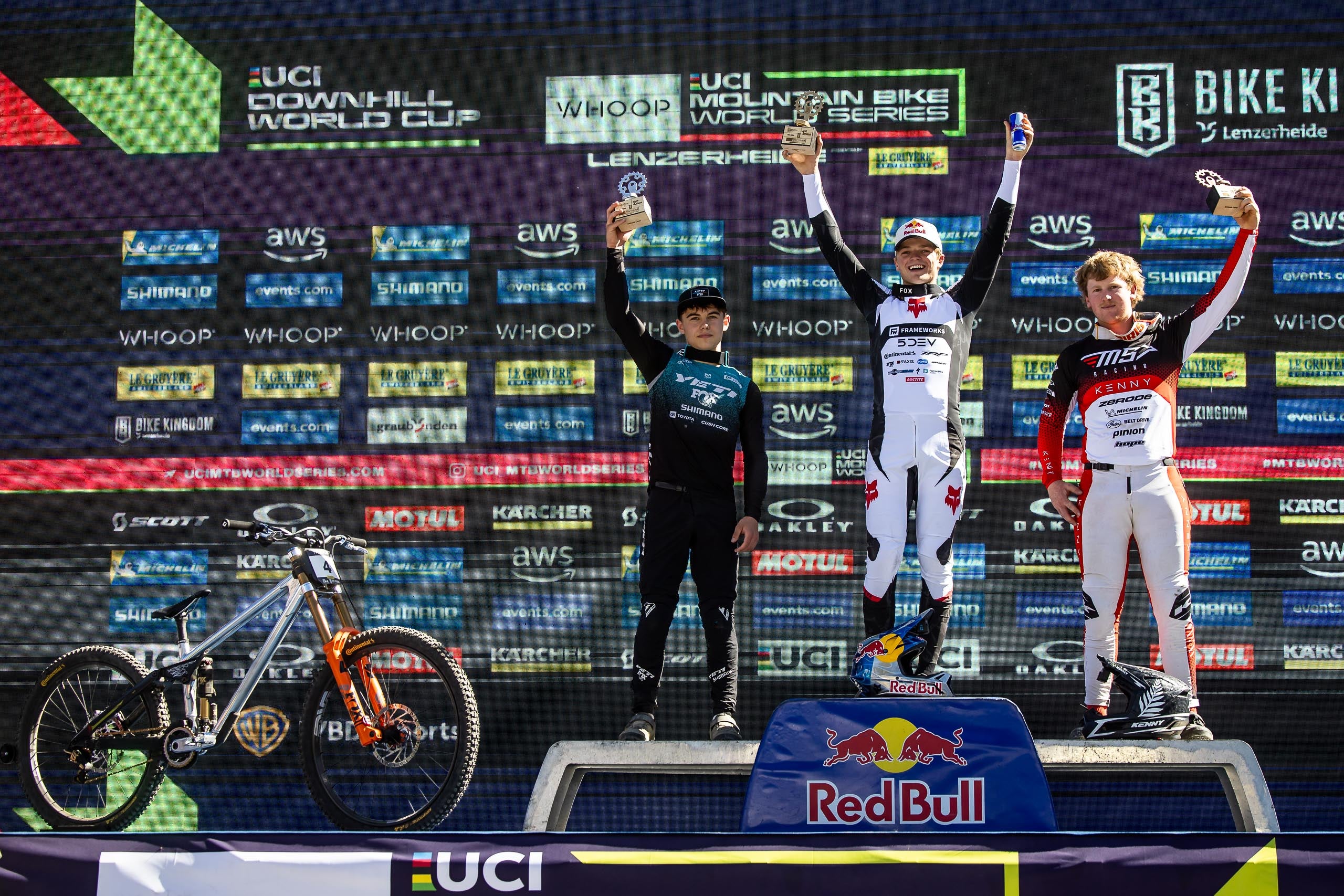 Three mountain bikers on a podium with UCI and Red Bull branding in the background.